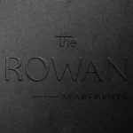The Rowan Apartments logo on textured surface.