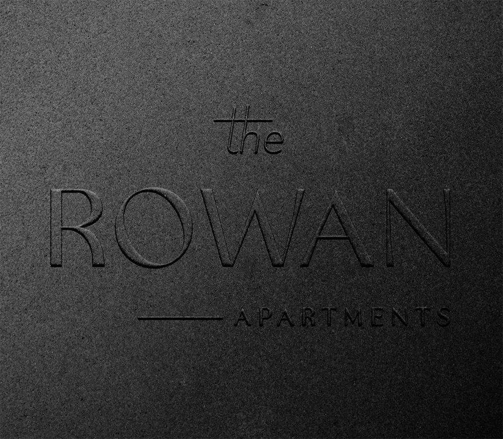 The Rowan Apartments logo on textured surface.
