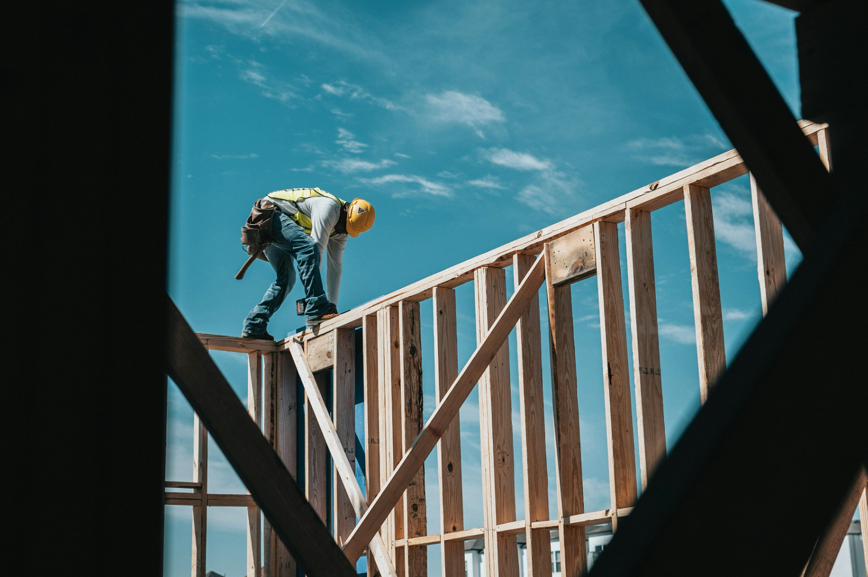 Construction worker on wooden house frame under blue sky